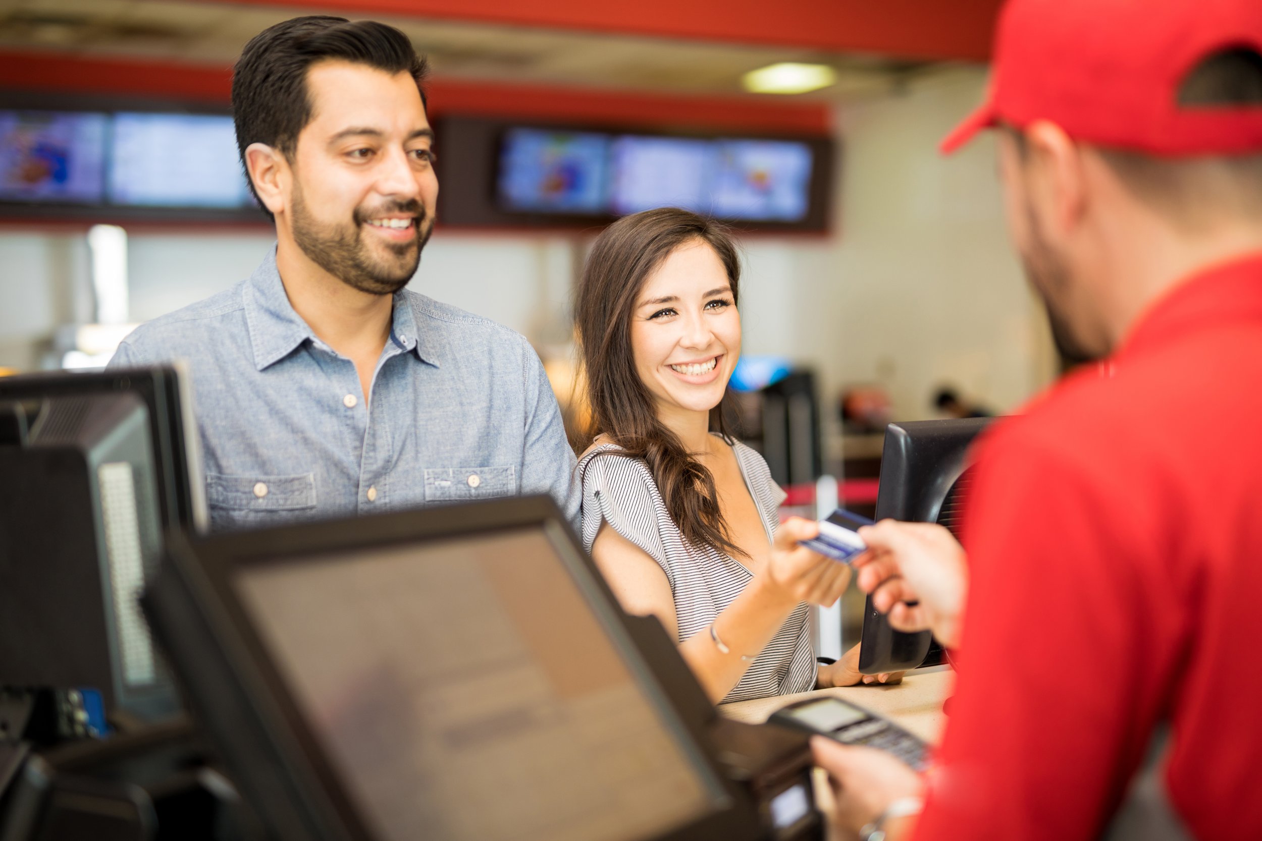 Portrait of a good looking Hispanic couple on a date at the movie theater while the woman pays for the tickets