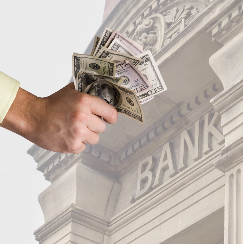 hand holding paper cash notes over faded image of a bank